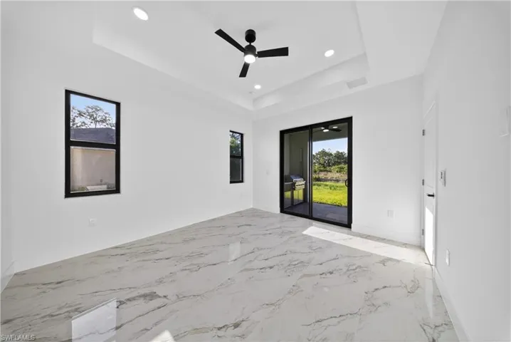 Unfurnished room featuring recessed lighting, ceiling fan, light marble finish floors, and a tray ceiling