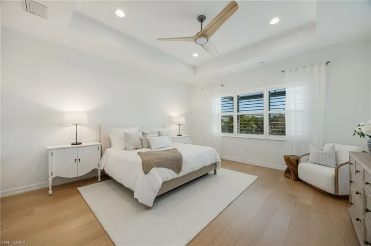 The primary bedroom features a double tray ceiling, wood flooring, and a large picture window overlooking the natural landscape and lake views.