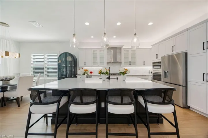 This kitchen! Clean lines, elegant light fixtures, wood flooring, textured tile backsplash, upgraded LG refrigerator, and cabinet pull-out trays, and island seating for 6 are just a few of the features that elevate this Sunrise home.