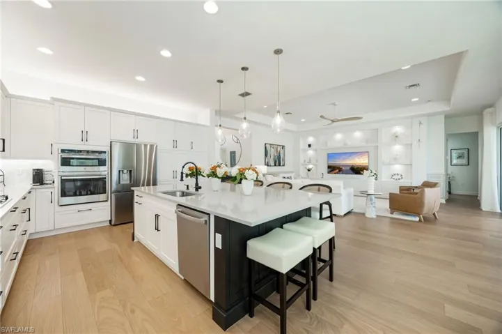 This kitchen! Clean lines, elegant light fixtures, wood flooring, textured tile backsplash, upgraded LG refrigerator, and cabinet pull-out trays, and island seating for 6 are just a few of the features that elevate this Sunrise home.