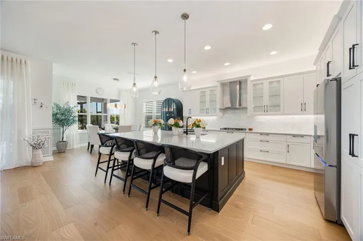 This kitchen! Clean lines, elegant light fixtures, wood flooring, textured tile backsplash, upgraded LG refrigerator, and cabinet pull-out trays, and island seating for 6 are just a few of the features that elevate this Sunrise home.
