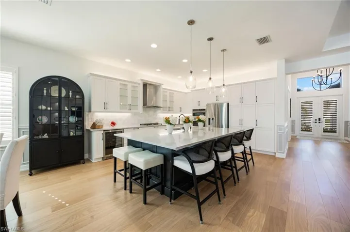 This kitchen! Clean lines, elegant light fixtures, wood flooring, textured tile backsplash, upgraded LG refrigerator, and cabinet pull-out trays, and island seating for 6 are just a few of the features that elevate this Sunrise home.