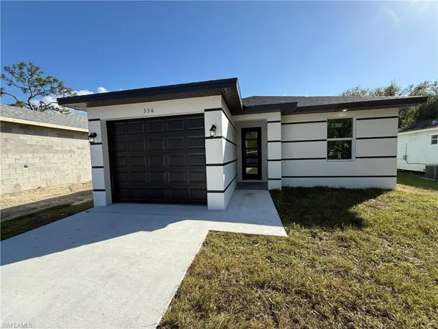 View of front of house with a front yard, central AC, and a garage