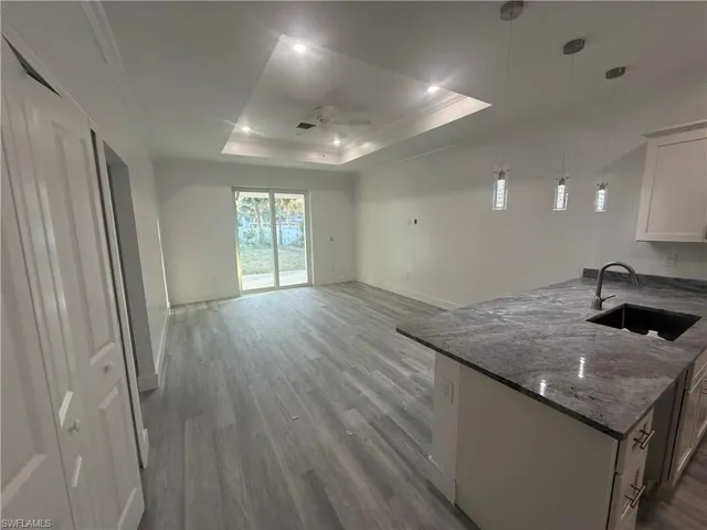 Kitchen featuring sink, white cabinetry, dark stone counters, pendant lighting, and light hardwood / wood-style flooring