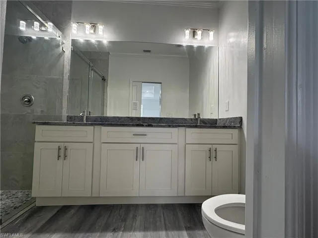 Bathroom featuring vanity, hardwood / wood-style floors, toilet, and a tile shower