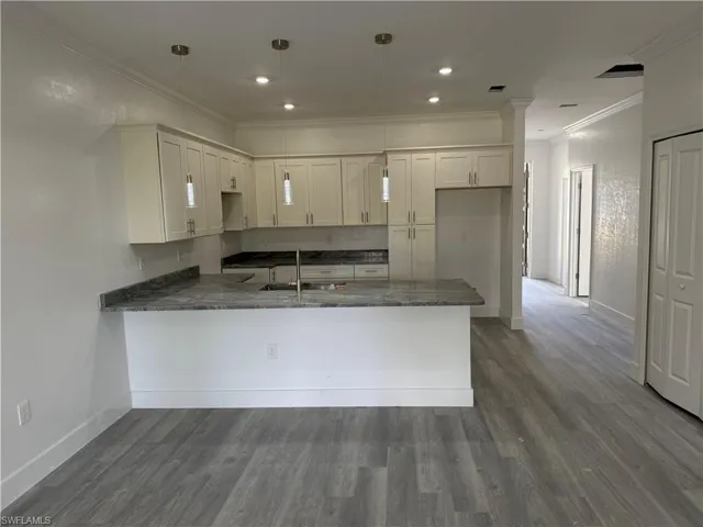 Kitchen with sink, kitchen peninsula, decorative light fixtures, white cabinets, and hardwood / wood-style flooring