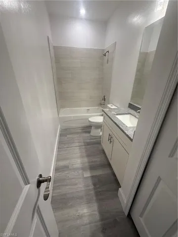 Full bathroom with vanity, toilet, hardwood / wood-style floors, and tiled shower / bath