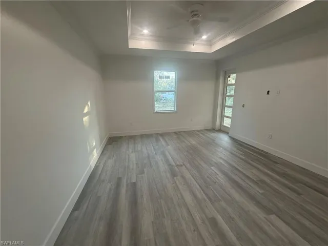 Spare room featuring dark hardwood / wood-style flooring, ornamental molding, ceiling fan, and a raised ceiling