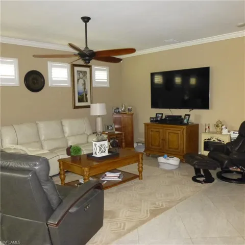 Tiled living room with ornamental molding, a healthy amount of sunlight, and ceiling fan