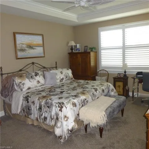 Carpeted bedroom featuring ornamental molding, ceiling fan, and a raised ceiling