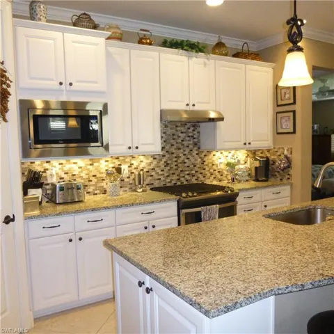 Kitchen featuring decorative backsplash, white cabinetry, hanging light fixtures, and appliances with stainless steel finishes