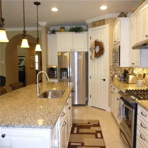 Kitchen with light tile patterned floors, an island with sink, stainless steel appliances, decorative light fixtures, and sink