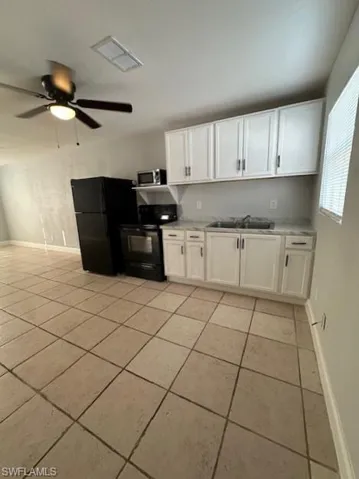 Kitchen with white cabinets, black appliances, light countertops, light tile patterned floors, and ceiling fan