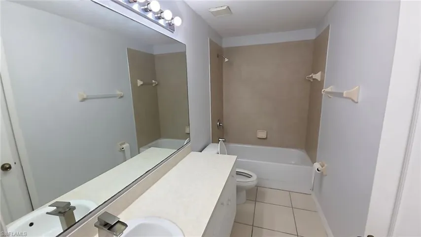 Bathroom featuring a vanity with an integrated sink, a large wall-mounted mirror, overhead bar lighting, a built-in bathtub with shower, and tiled flooring
