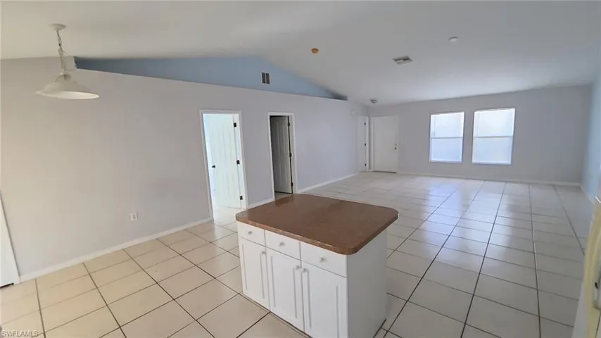 Spacious open-concept interior featuring light tile flooring and a central kitchen island with white cabinetry and a contrasting countertop