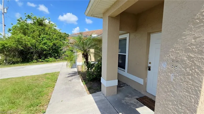 Front entry featuring a stucco exterior, covered porch, white paneled door, and a single window with white trim