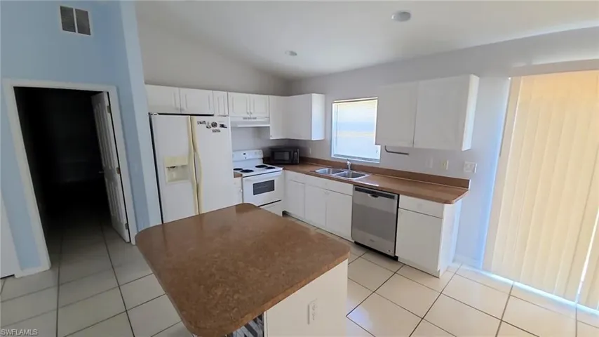 Kitchen featuring white cabinetry, a central island with a solid surface countertop, tile flooring, a stainless steel dishwasher, and a double basin sink
