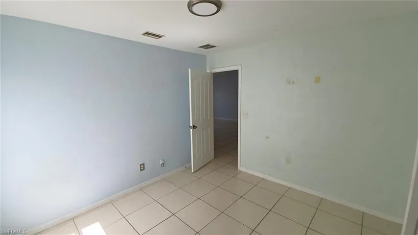 Interior room featuring light-colored tile flooring, a white baseboard, a ceiling-mounted flush light fixture, and an open doorway revealing an interior space