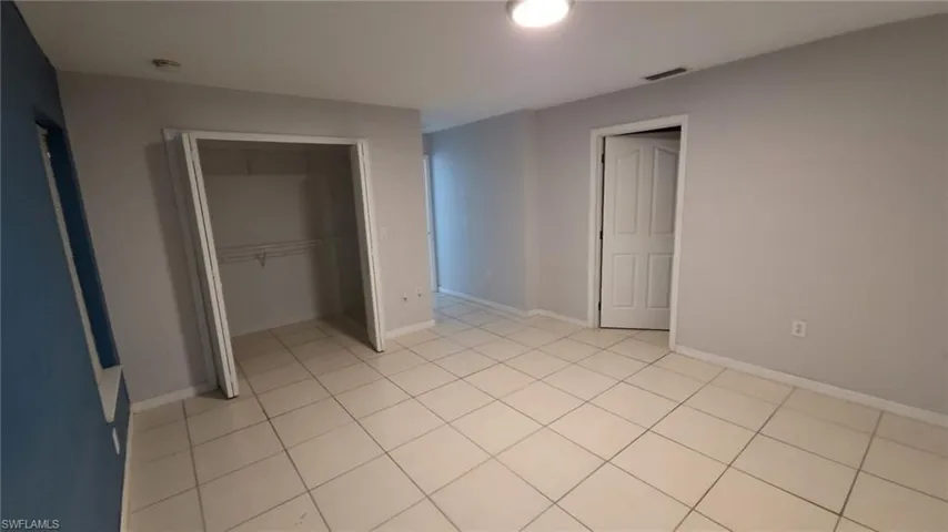 Spacious room featuring light tile flooring, neutral wall tones, a built-in closet with shelving, and a panel door