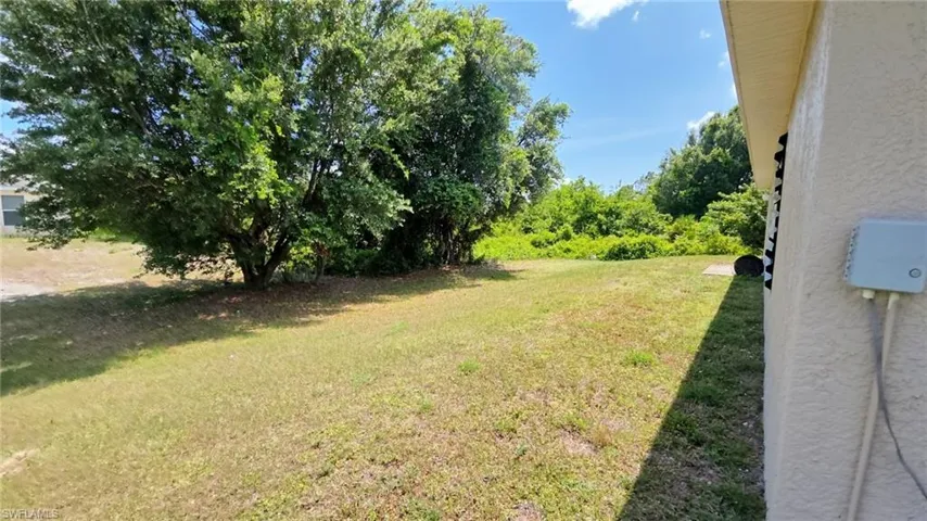 Expansive grass lawn featuring mature trees and a concrete patio pad