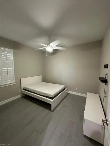 Room featuring wood-finish flooring, a ceiling fan with integrated lighting, and window with white plantation shutters
