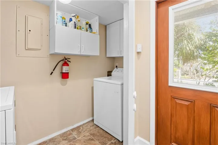 Laundry area featuring cabinet space, electric panel, washing machine and dryer, and stone finish flooring