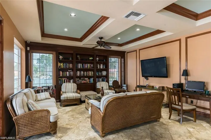 Living room with ceiling fan, a raised ceiling, ornamental molding, and light tile patterned floors