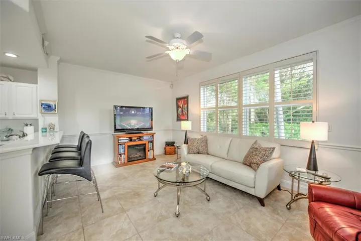 Living area with ornamental molding, ceiling fan, a glass covered fireplace, and light tile patterned floors