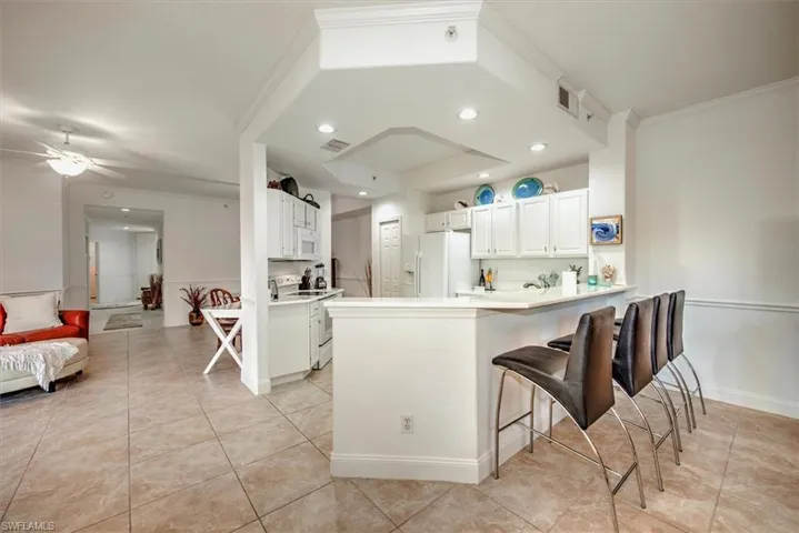 Kitchen featuring white cabinets, light countertops, white appliances, a peninsula, and light tile patterned floors