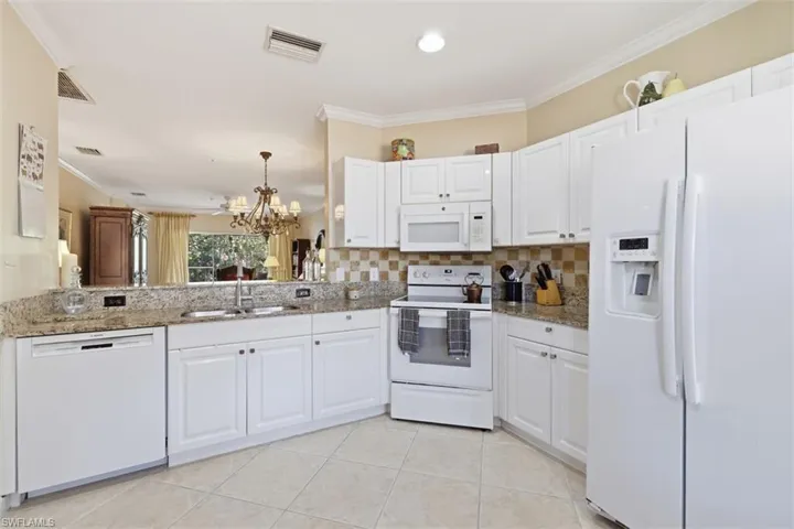 Kitchen with white appliances, ornamental molding, light stone counters, hanging lights, and white cabinets