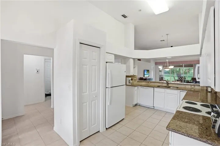 Kitchen featuring white appliances, light tile patterned floors, dark stone counters, decorative light fixtures, and white cabinetry