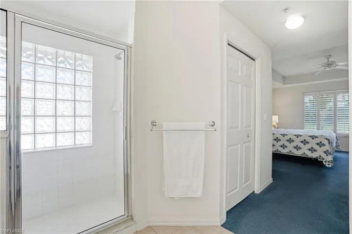 Full bath featuring ensuite bath, a ceiling fan, a shower stall, light carpet, and a closet
