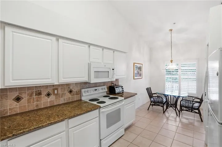 Kitchen featuring white appliances, white cabinets, backsplash, light tile patterned floors, and decorative light fixtures