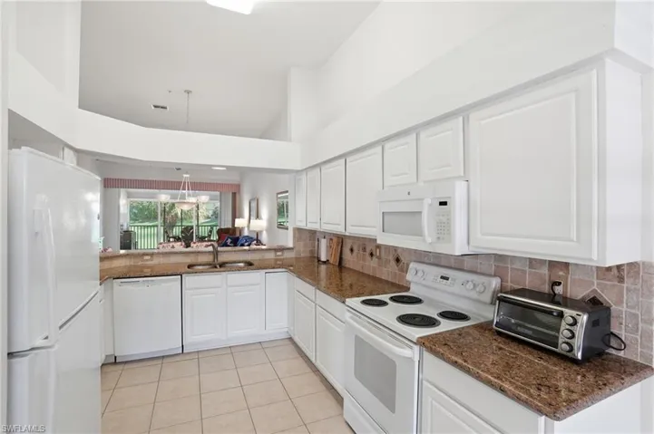 Kitchen with white appliances, hanging light fixtures, white cabinets, dark stone countertops, and lofted ceiling