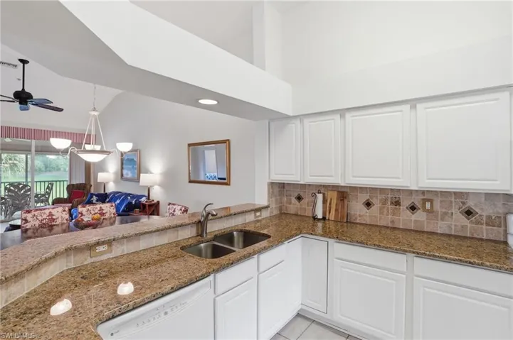 Kitchen with dark stone countertops, dishwasher, open floor plan, tasteful backsplash, and white cabinetry