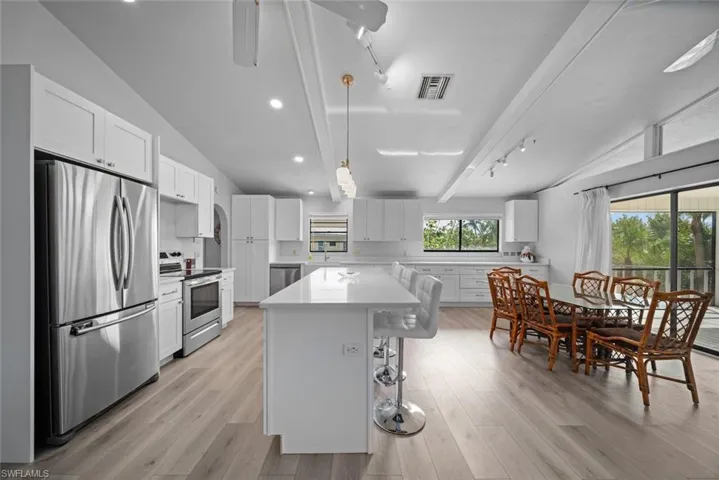 Kitchen with appliances with stainless steel finishes, vaulted ceiling, a center island, white cabinets, and light countertops