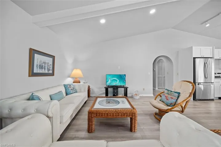 Living room with lofted ceiling, arched walkways, light wood-style flooring, baseboards, and recessed lighting