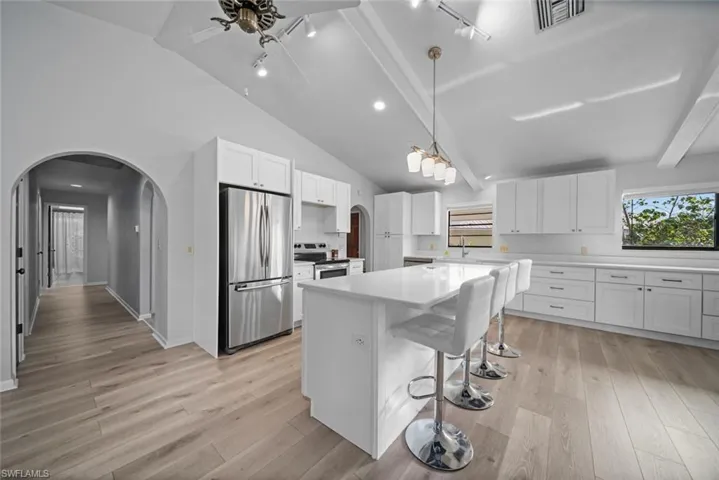 Kitchen featuring stainless steel appliances, arched walkways, rail lighting, white cabinetry, and lofted ceiling