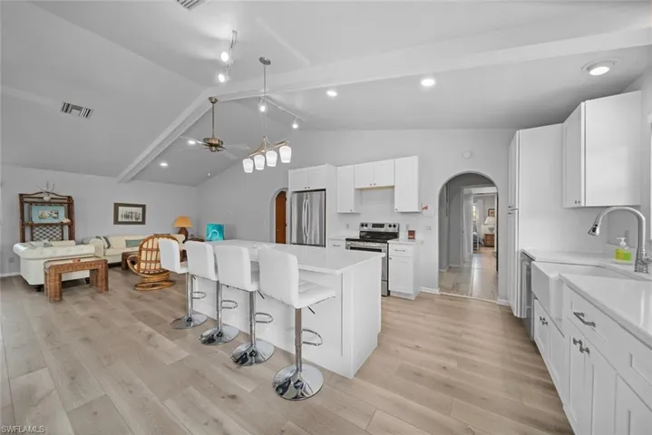Kitchen featuring arched walkways, appliances with stainless steel finishes, a sink, a breakfast bar area, and light wood finished floors
