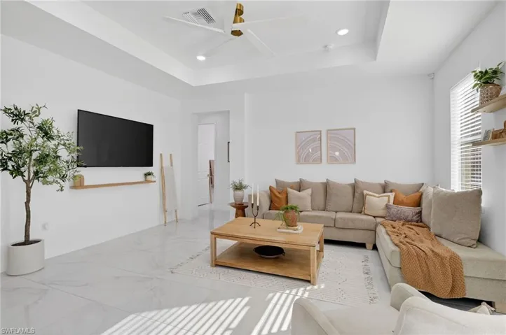 Living area with a tray ceiling, recessed lighting, a ceiling fan, and marble finish flooring