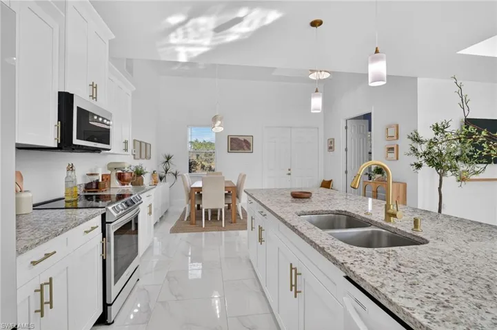 Kitchen with stainless steel appliances, pendant lighting, white cabinets, and light stone countertops