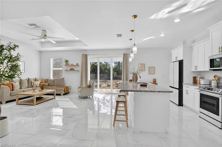Kitchen with stainless steel appliances, light stone countertops, a breakfast bar, an island with sink, and light marble finish flooring