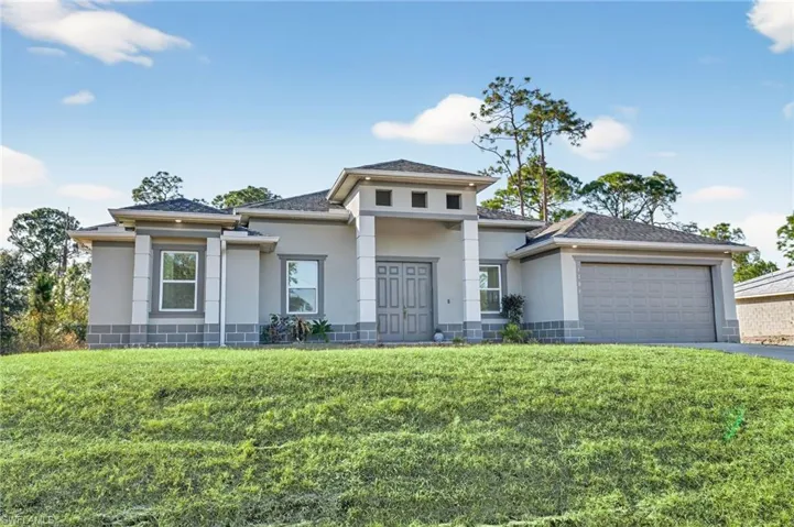 Prairie-style home with stucco siding, a front yard, an attached garage, and driveway