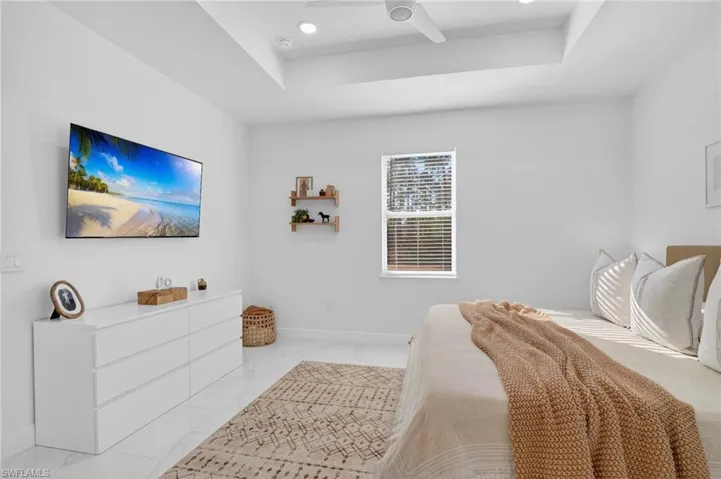 Bedroom with a tray ceiling, recessed lighting, marble look tile flooring, and a ceiling fan