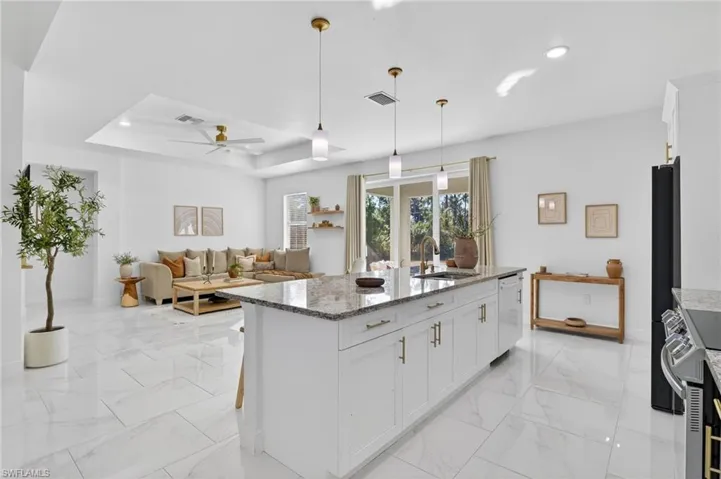 Kitchen featuring light stone counters, white cabinets, stainless steel electric stove, and a raised ceiling