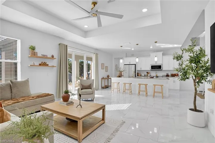 Living room with a raised ceiling, a ceiling fan, light marble finish floors, and recessed lighting