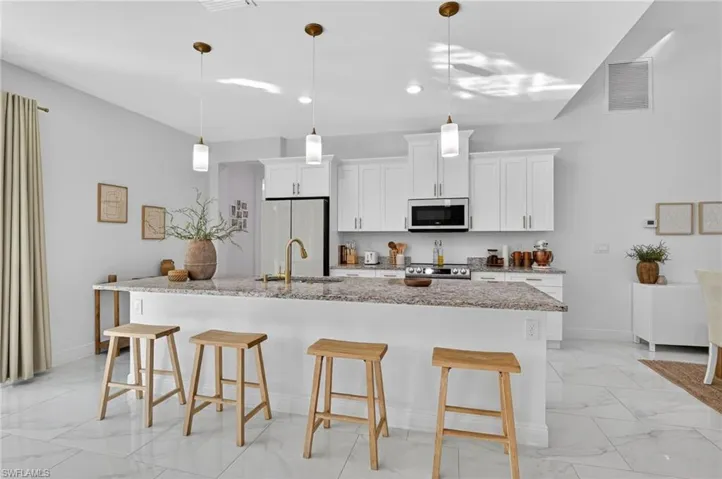 Kitchen with a kitchen bar, light marble finish flooring, white cabinets, light stone countertops, and a center island with sink