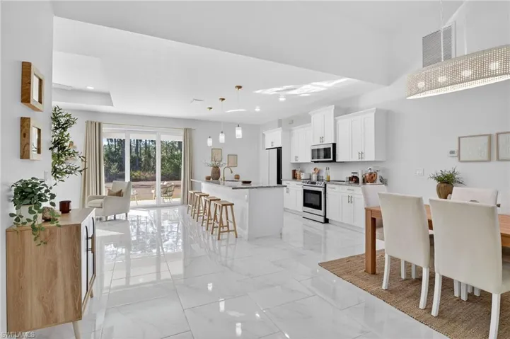 Kitchen featuring a breakfast bar area, pendant lighting, stainless steel appliances, a kitchen island with sink, and white cabinets