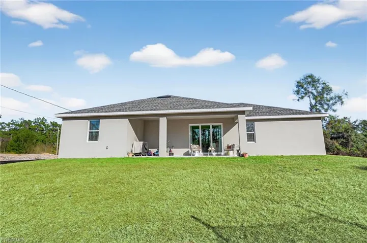 Back of property with stucco siding, roof with shingles, a patio area, and a yard