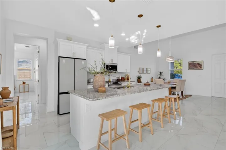 Kitchen with white cabinets, light stone countertops, a breakfast bar area, stainless steel appliances, and a center island with sink